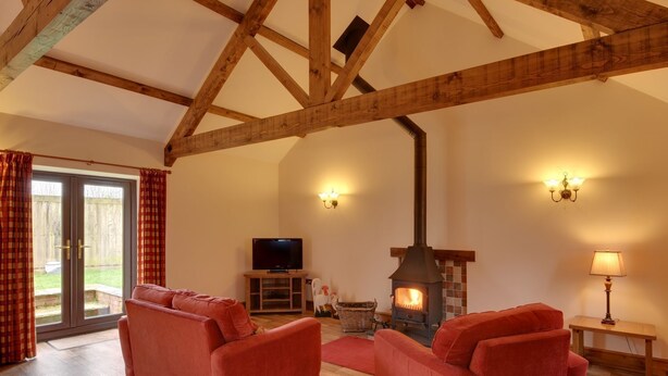 Ein Wohnzimmer mit Holzbalken, einem Kamin, einem Fernseher und zwei roten Sofas.