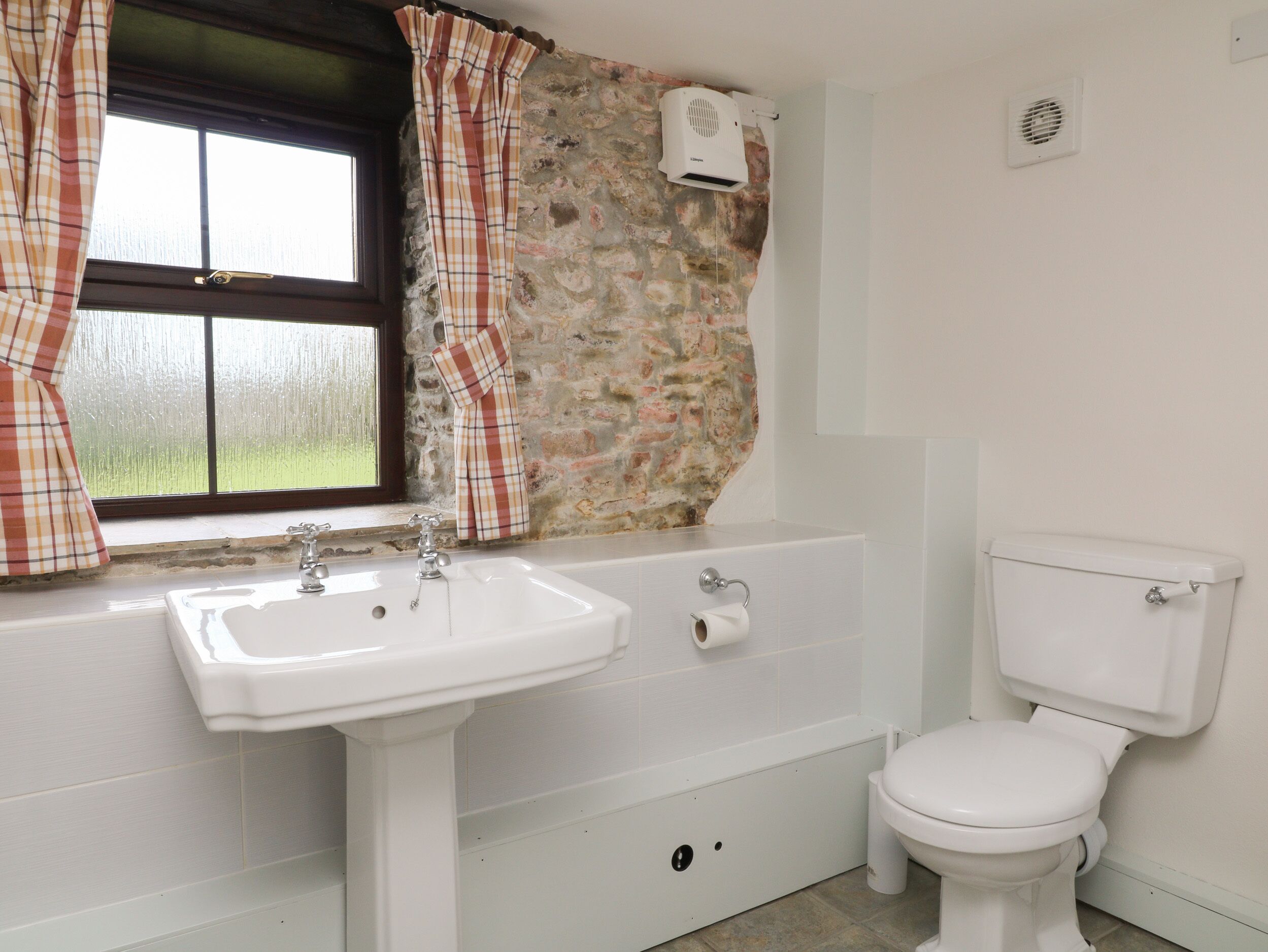 A bathroom with a white sink, a toilet, and a window with plaid curtains.