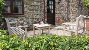 Un edificio de piedra con puerta y ventana de madera, con mesas y sillas para exteriores y una maceta con flores.