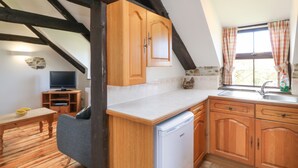 Una cocina con armarios de madera, lavavajillas integrado, pared de piedra y ventana con cortinas.
