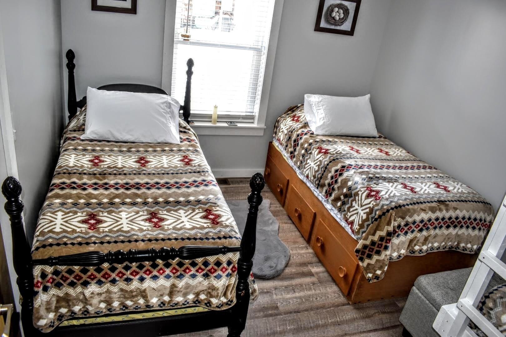 A bedroom with two single beds, a window with blinds, a wooden floor, and a small rug.