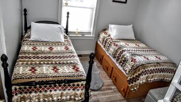 A bedroom with two single beds, a window with blinds, a wooden floor, and a small rug.