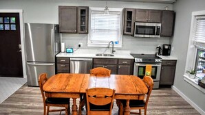 Una cocina moderna con una mesa de comedor de madera, electrodomésticos de acero inoxidable y muebles de cocina oscuros.