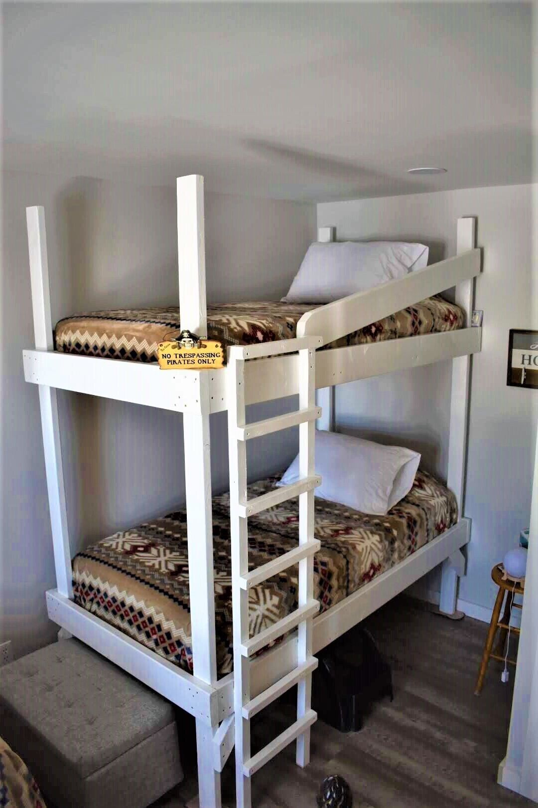 Una cama litera con escalera, un taburete pequeño y un cuadro en la pared.