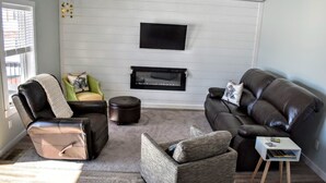 Una sala de estar con chimenea, sofás de cuero, una mesita auxiliar y un sillón verde.