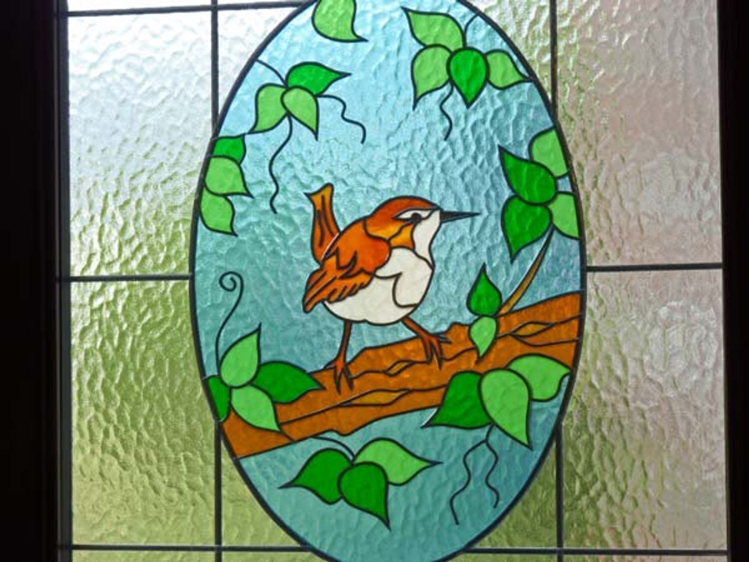 Un vitrail représentant un oiseau perché sur une branche, entouré de feuilles vertes.