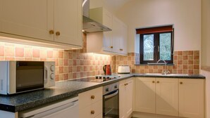 Une cuisine compacte avec des meubles blancs, un four à micro-ondes encastré, une cuisinière à gaz et une fenêtre avec des stores.