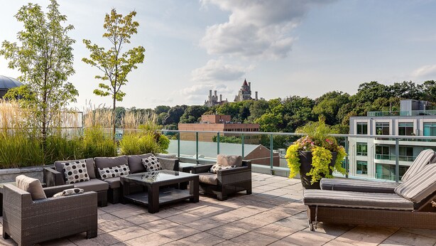 A rooftop terrace with wicker furniture, a view of a castle, and a modern building in the background.