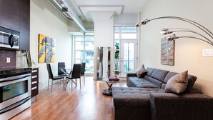 A modern kitchen with a built-in oven and microwave, a dining area with a glass table and chairs, and a living room with a sofa and decorative pillows.