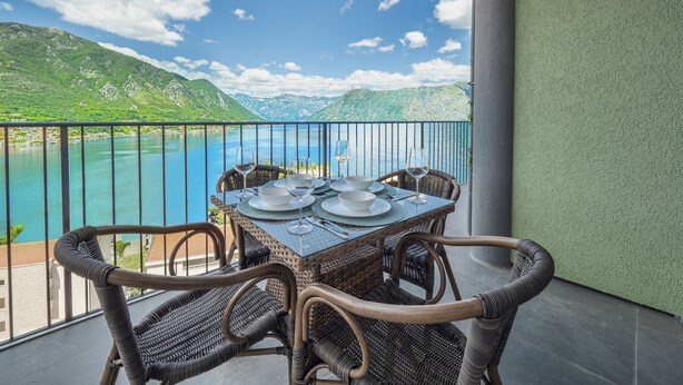 A balcony with a table set for dining, overlooking a lake and mountains. - Luxurious Apartment with Captivating Majestic View (Dobrota)
