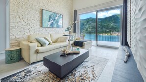 A modern living room with a beige sofa, a dark coffee table, and a large window offering a mountain view. - Luxurious Apartment with Captivating Majestic View (Dobrota)
