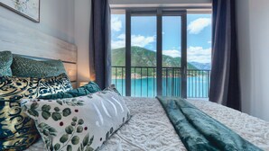 A bedroom with a large bed, a view of a coastal area, and a balcony with a railing. - Luxurious Apartment with Captivating Majestic View (Dobrota)