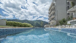 A swimming pool with blue mosaic tiles, surrounded by a modern building with balconies and a mountain view in the background. - Luxurious Apartment with Captivating Majestic View (Dobrota)
