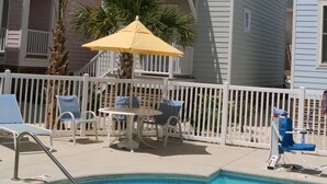 A pool area with lounge chairs and umbrellas, surrounded by a white fence.