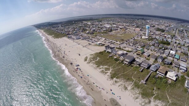 An aerial view of a coastal town with a beach, residential areas, and a water tower.
