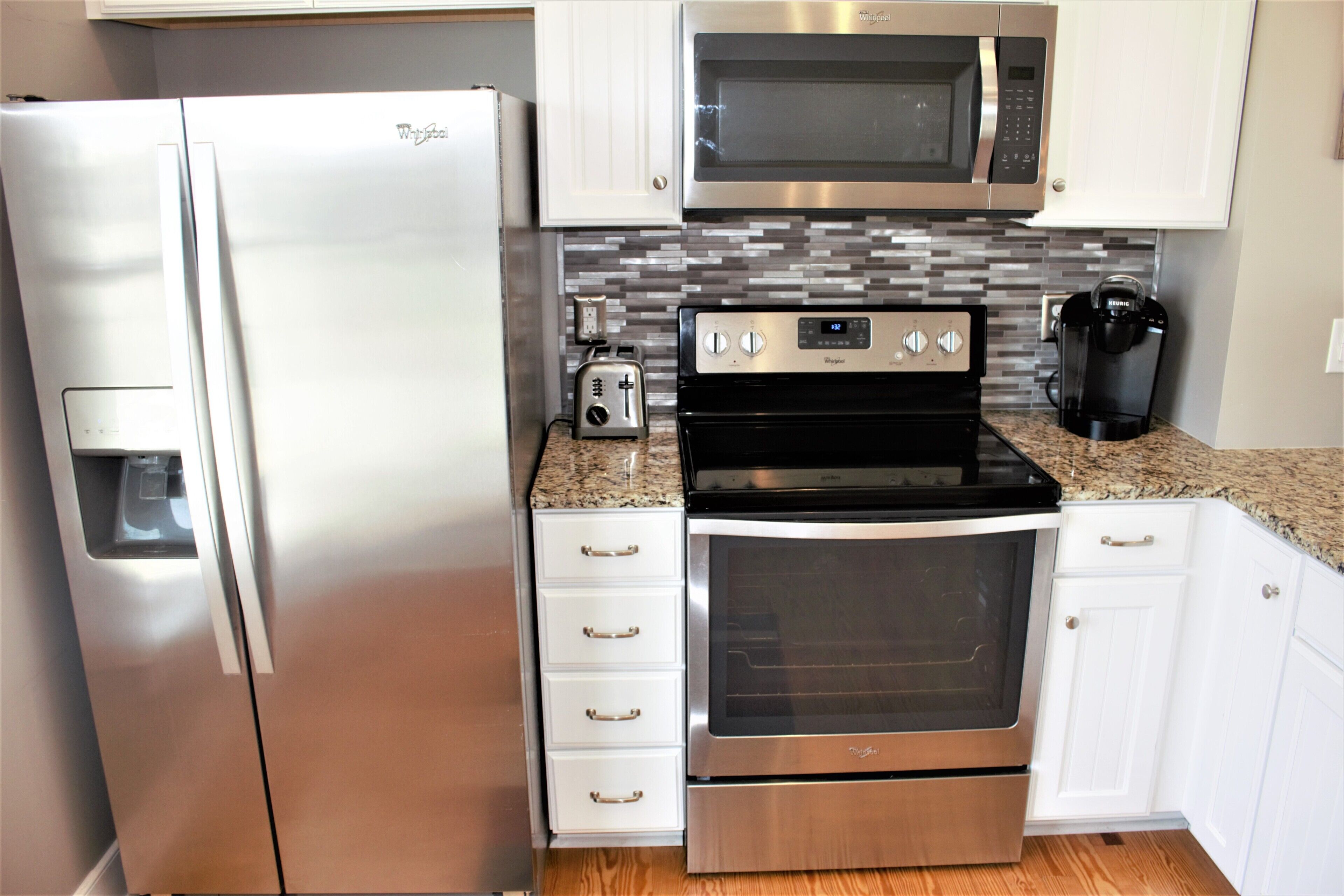 A compact kitchen with a stainless steel refrigerator, a microwave, a toaster, an oven, and a coffee maker.