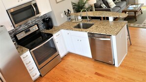 A compact kitchen with a microwave, oven, and dishwasher, adjacent to a living area with a sofa and coffee table.