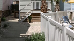 A two-story building with a balcony, a wooden deck, and a small garden area with palm trees.