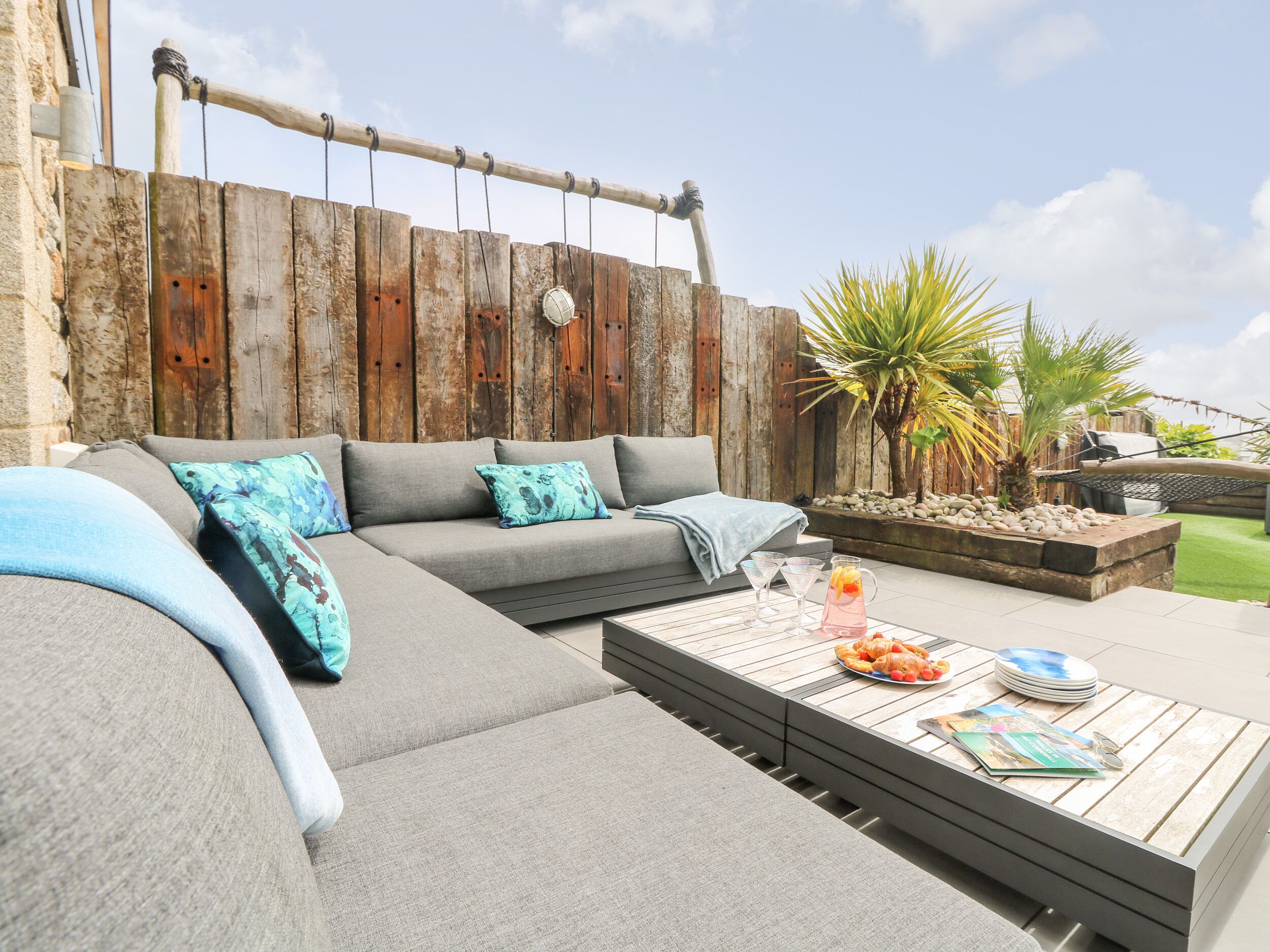 A modern outdoor seating area with a grey sofa, a wooden coffee table, and a grill.