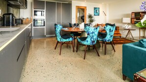A modern kitchen with a dining area, featuring a large island, dark blue chairs, and a teal sofa.