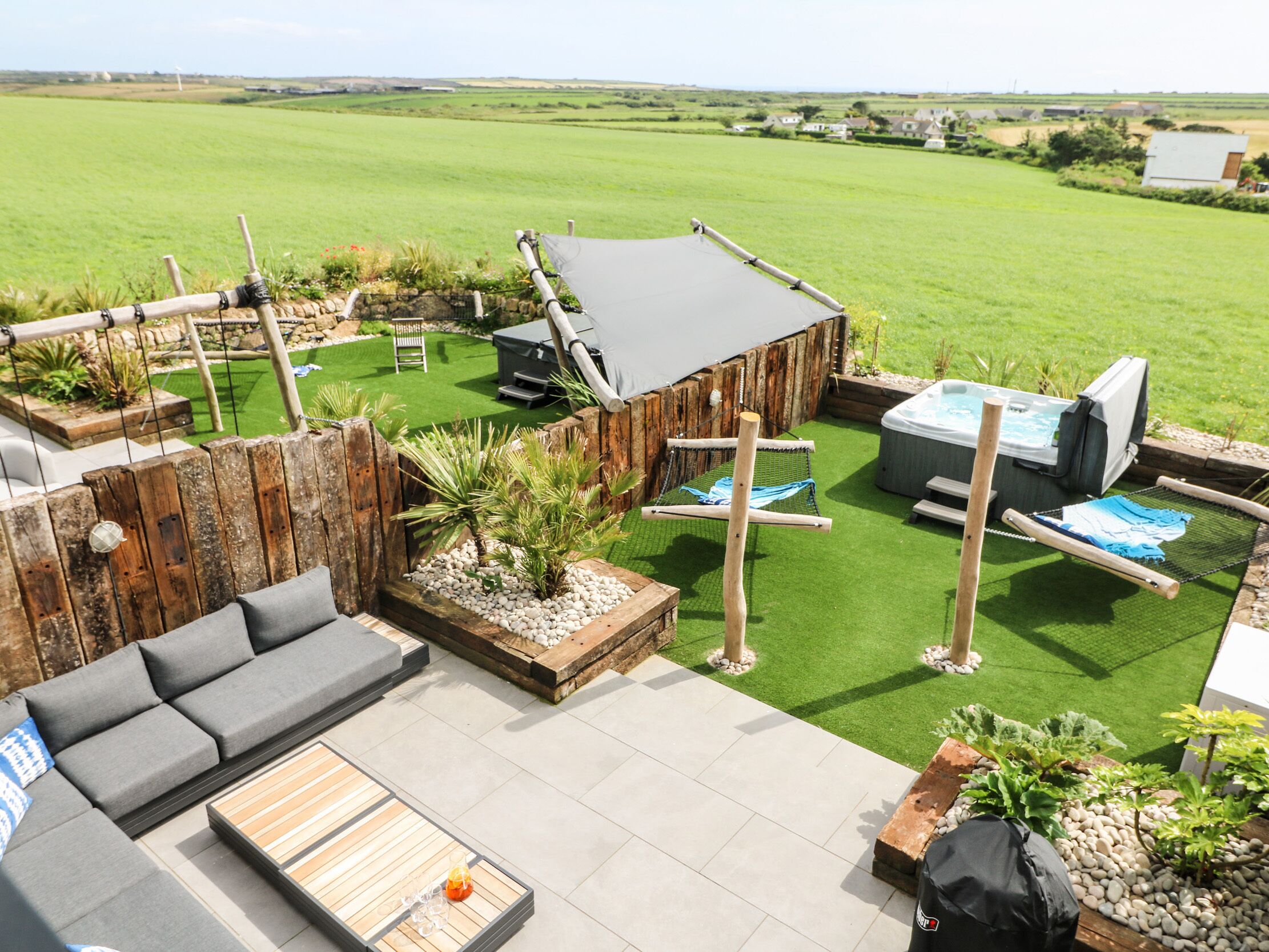 Eine Terrassenanlage mit Holzdeck, Gartenmöbeln, einem Whirlpool und Blick ins Grüne.