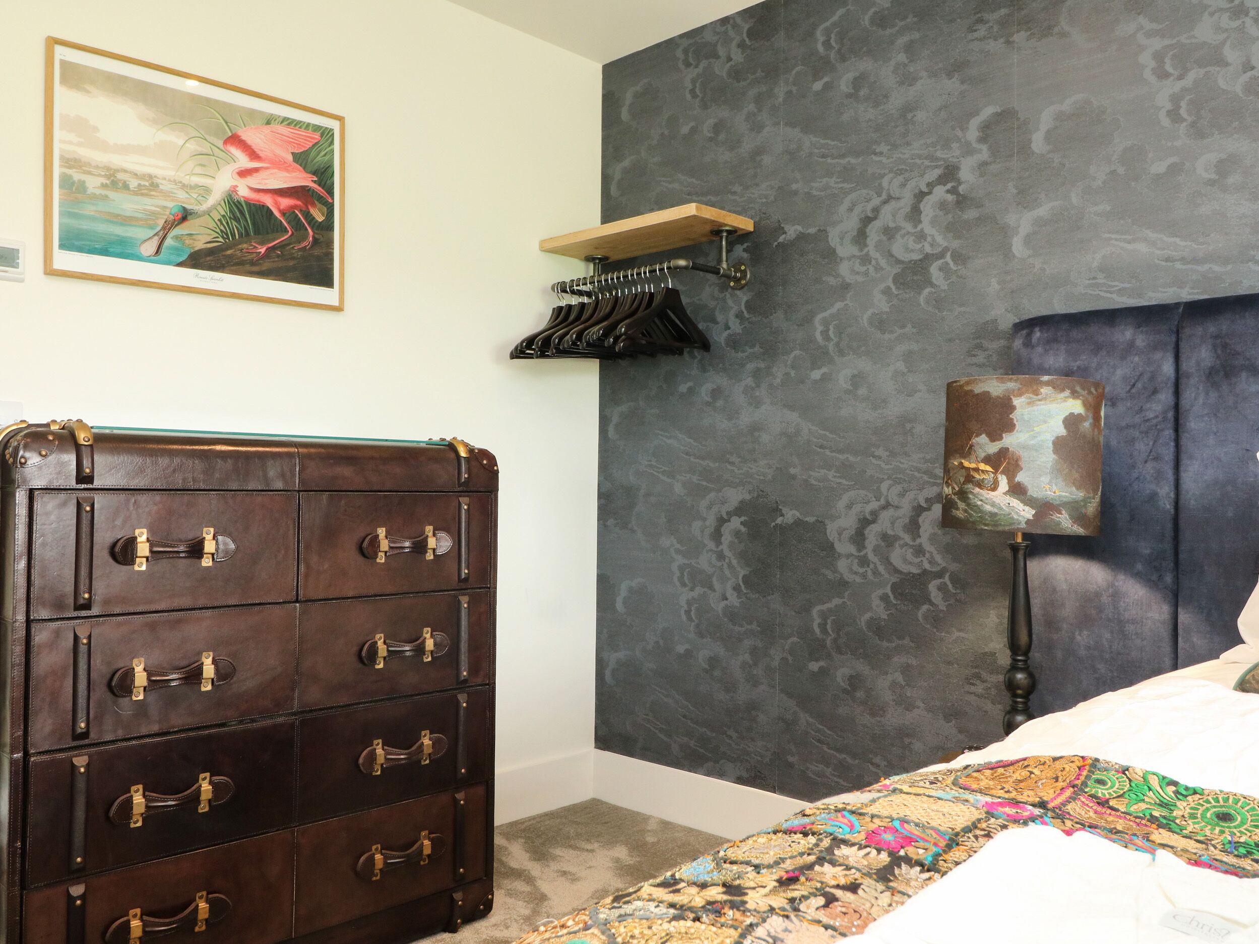 Un dormitorio con un aparador de madera grande, una pared gris con textura, un cuadro enmarcado y una lámpara.