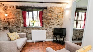 A cozy living room with a stone wall, a white radiator, a flat-screen TV on a stand, and two sofas with patterned cushions. - Wagtail (Holsworthy)