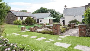 A courtyard with stone pathways, a central seating area with a table and chairs, and surrounding buildings with stone and tiled roofs. - Wagtail (Holsworthy)