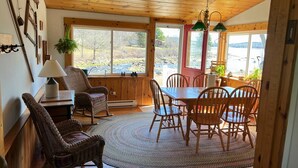 A cozy dining area with wooden furniture, a large window offering a view of a natural landscape, and a ceiling with exposed beams.