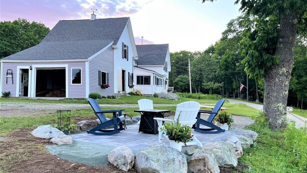 A house with a porch, two Adirondack chairs, a table, and a potted plant.