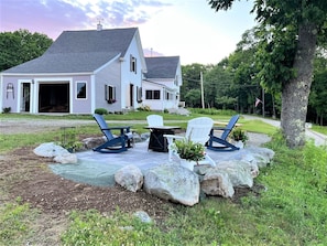 Une maison avec une véranda, deux fauteuils Adirondack, une table et un pot de fleurs.