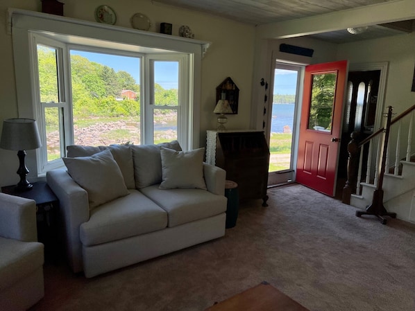 Un salon avec un canapé beige, une lampe et une vue sur un lac, visible à travers de grandes fenêtres.
