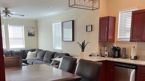 Eine moderne Küche mit Geschirrspüler, ein Essbereich mit Holztisch und -stühlen sowie ein Wohnzimmer mit Sofa und Deckenventilator.