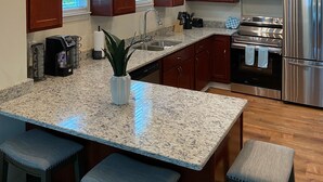 Eine moderne Küche mit Granit-Arbeitsplatten, Edelstahlgeräten, Holzschränken und einer Bar mit Hockern.