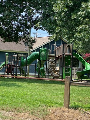Kids can play on the playground's green slide, climbing elements, and small bridge.