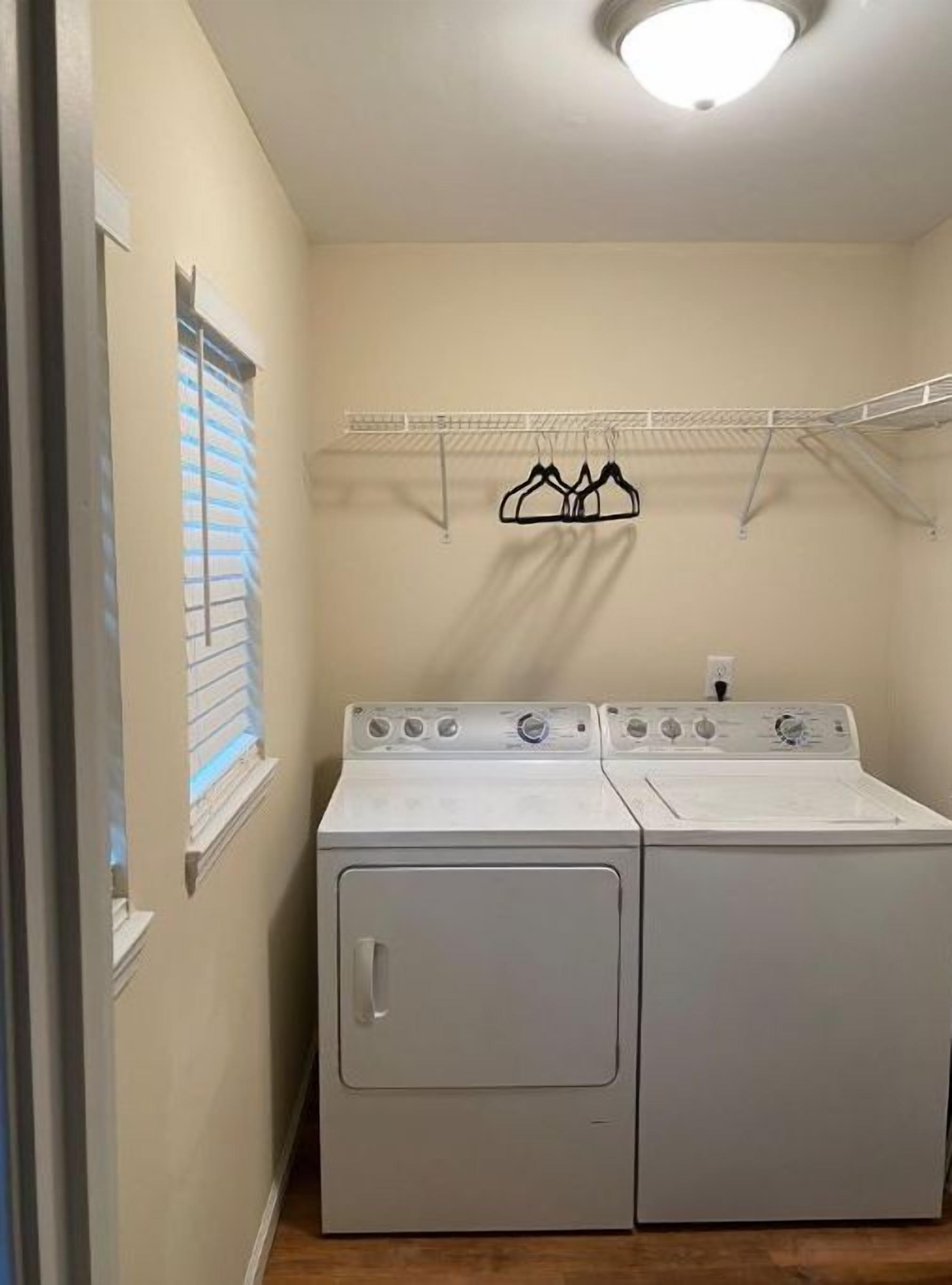Une buanderie équipée d’un lave-linge et d’un sèche-linge à chargement frontal, d’un étendoir et d’une fenêtre avec des stores.
