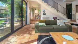 Una sala de estar moderna con un sofá verde, una mesa de centro de madera y una escalera que conduce a un nivel superior.