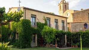 Un edificio con un campanario, paredes cubiertas de hiedra y un patio con mobiliario exterior.