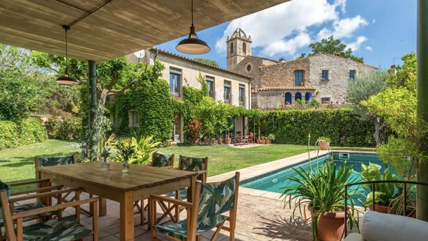 Un patio exterior con piscina, una mesa y sillas, y vistas de un edificio histórico con una torre de campanas.