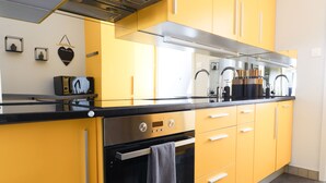 Een keuken met gele kastjes, een zwart aanrecht, roestvrijstalen apparatuur en een moderne kraan.
