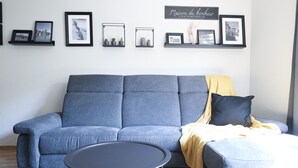 Een moderne woonkamer met een grijze bank, een klein rond tafeltje en een gele plaid.
