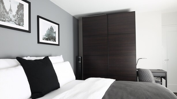 Een moderne hotelkamer met een groot bed, een donkere inbouwkast en twee afbeeldingen in lijsten aan de muur.
