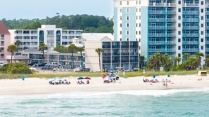 Um hotel à beira-mar com vários andares, varandas e uma área de praia com guarda-sóis e espreguiçadeiras.