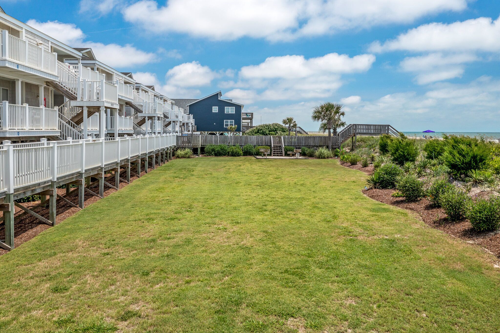 A coastal property with a grassy lawn, wooden deck, and a large house with balconies.
