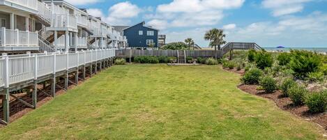 A coastal property with a grassy lawn, wooden deck, and a large house with balconies.
