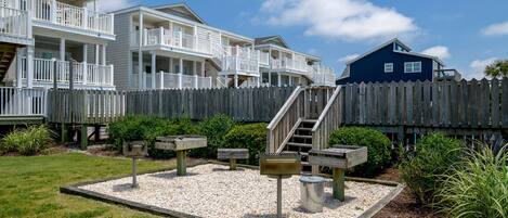 A beachfront property with multiple-story buildings, a wooden fence, and a landscaped garden with benches and mailboxes.
