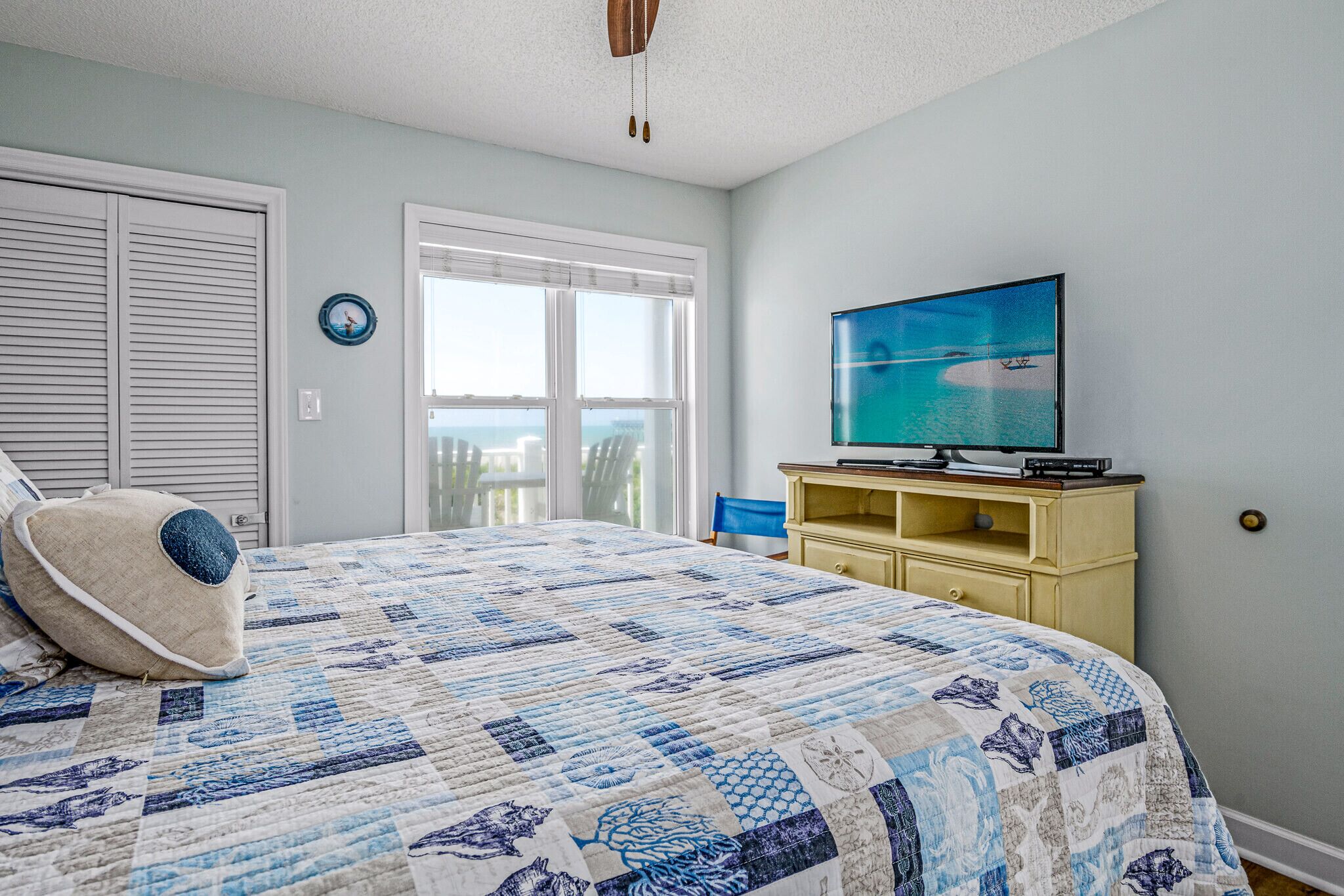 Quarto com cama grande, televisão sobre suporte de madeira e vista para o oceano através de uma janela.