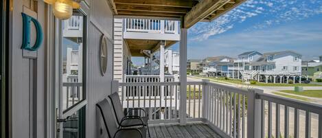 A wooden deck with two chairs and a table, overlooking a row of houses.