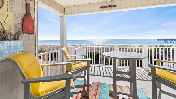 A covered outdoor seating area with white furniture and a view of the beach. - "Waters Edge 435-A" - Oceanfront Condo w/ Community Pool, 2 Bedrooms / 2 Bathrooms (Holden Beach)