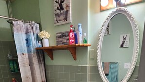 A bathroom with a toilet, sink, and bathtub. There is a shower curtain, a mirror, and a shelf with toiletries. - Apartment Attached to a 1900 historic Farm house (Old Mill Creek)